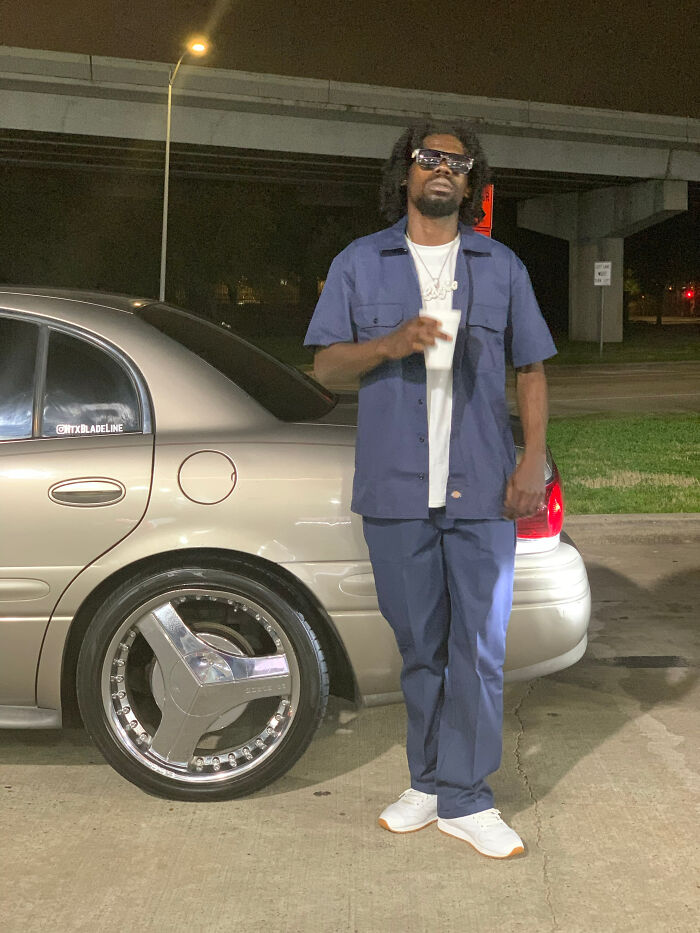 A man in a blue uniform and sunglasses standing next to a car at night, exhibiting surprising facts.