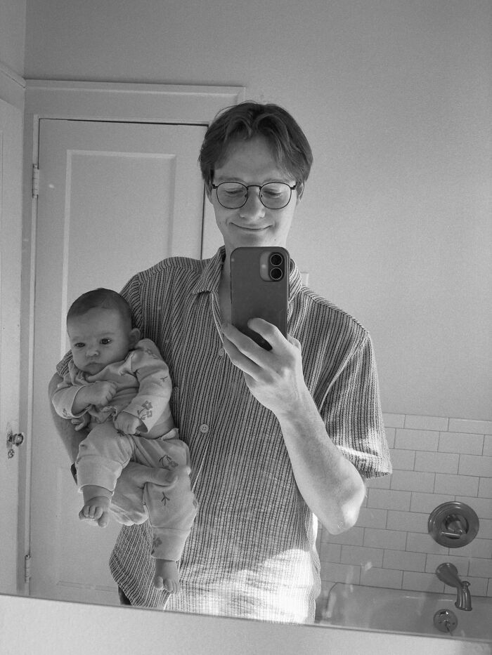 A black and white photo of a man holding a baby, taking a mirror selfie, sharing surprising facts.