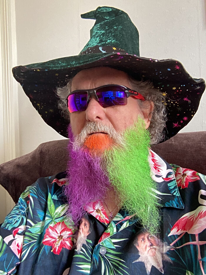 A man with a colorful beard in orange, purple, and green, wearing a wizard hat and sunglasses, showing surprising facts.