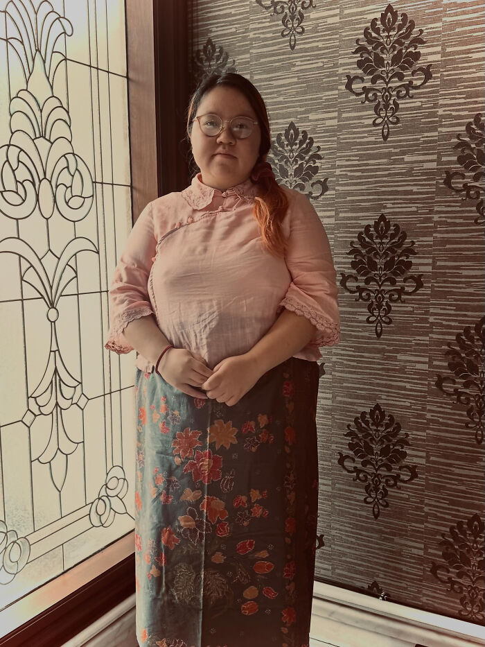 A woman in a pink blouse and floral skirt stands indoors, highlighting surprising facts about people's looks.
