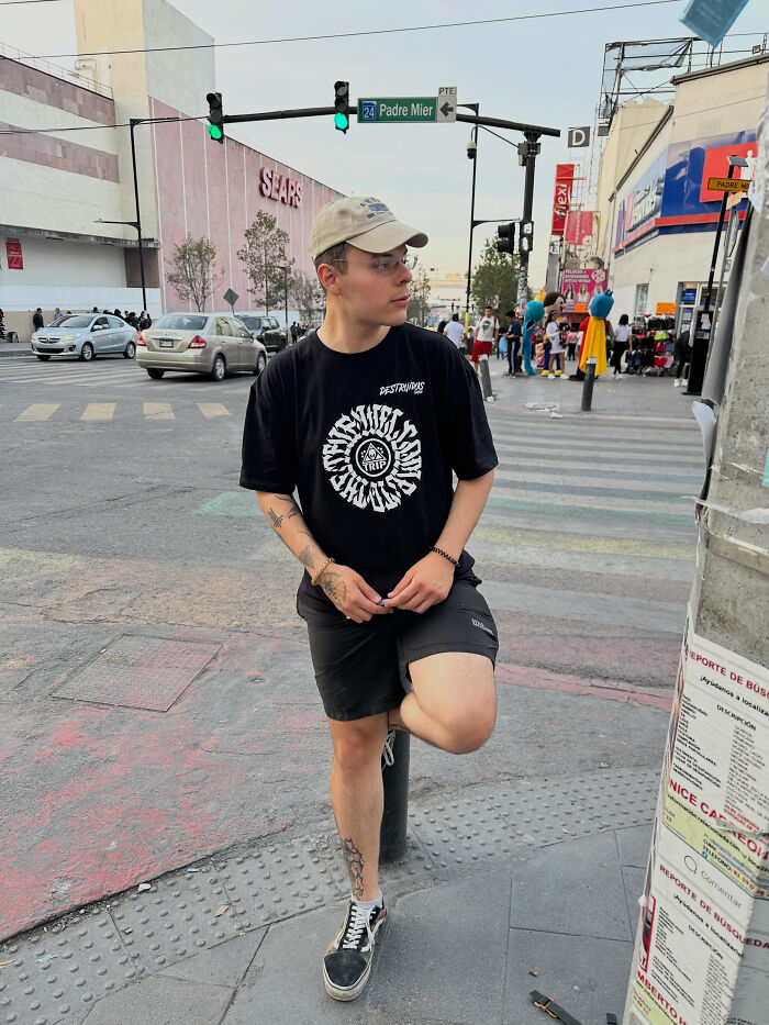 A young man in a black t-shirt and cap stands on a city street, revealing surprising facts about people's looks.
