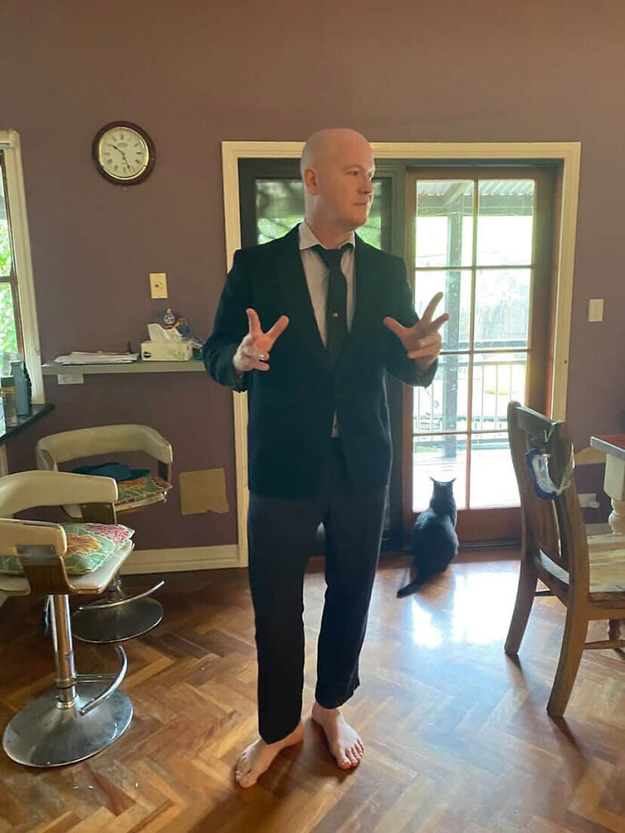 A man in a suit and tie, barefoot in his home, displays surprising facts about people's looks.