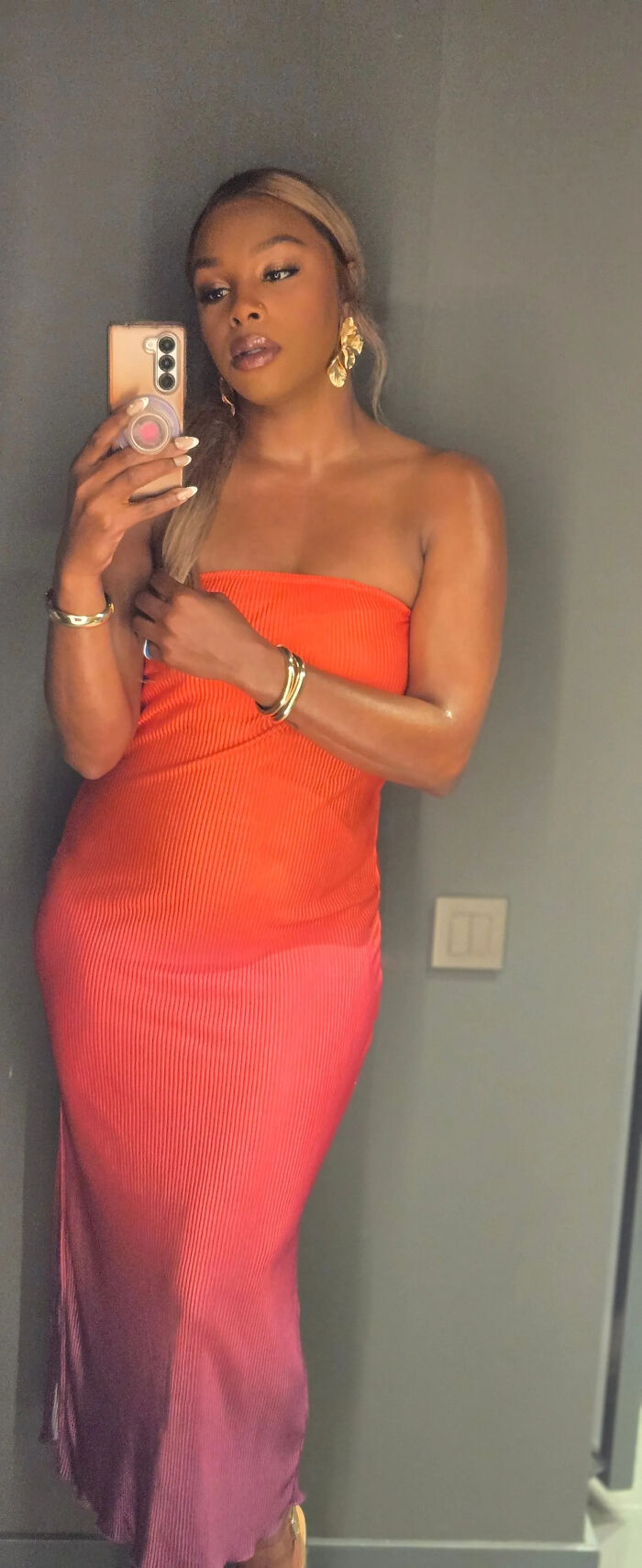 A woman in an orange strapless dress takes a selfie, showcasing surprising facts about people's looks.