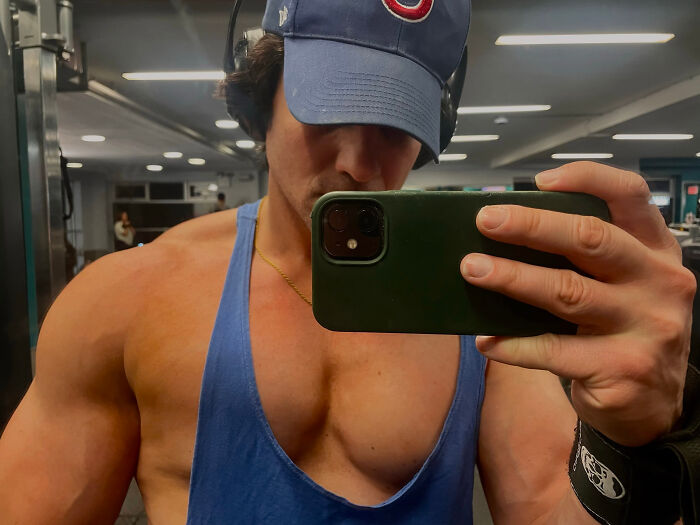 Man in a blue tank top, baseball cap, and headphones, flexing in a gym, showing surprising facts.