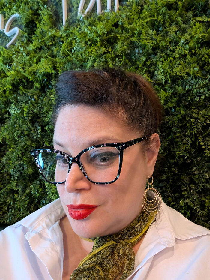 A woman with surprising facts about her looks, wearing cat-eye glasses, red lipstick, and a white shirt.