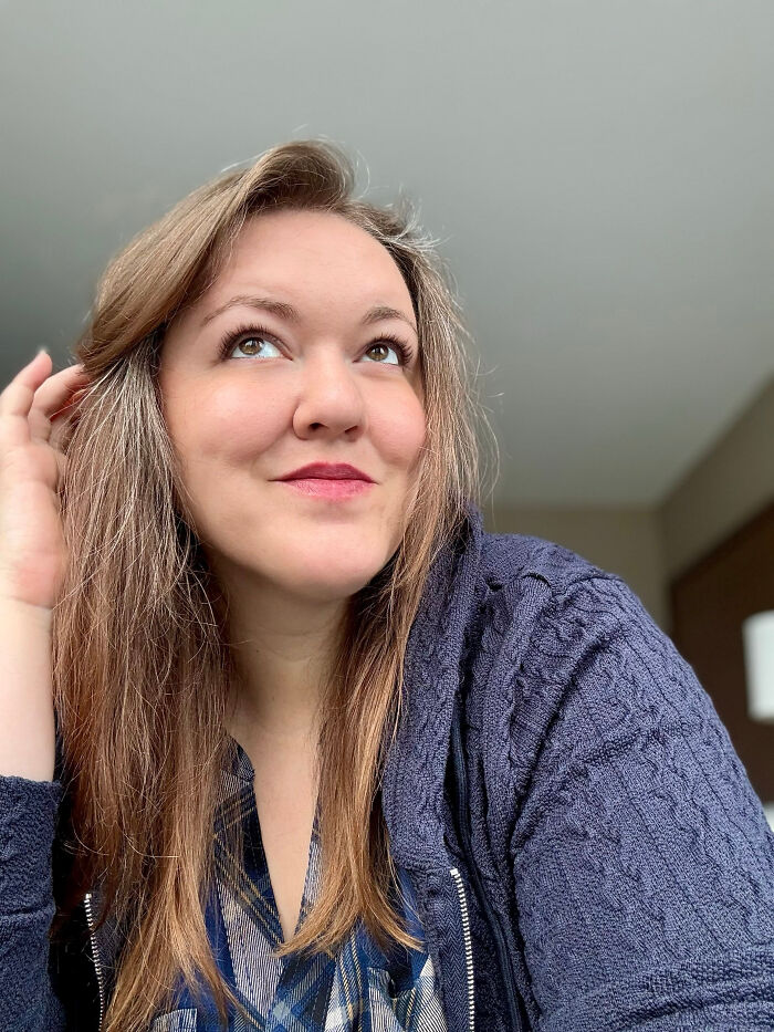 A woman with surprising facts about her looks, looking up with a thoughtful expression, wearing a patterned shirt.