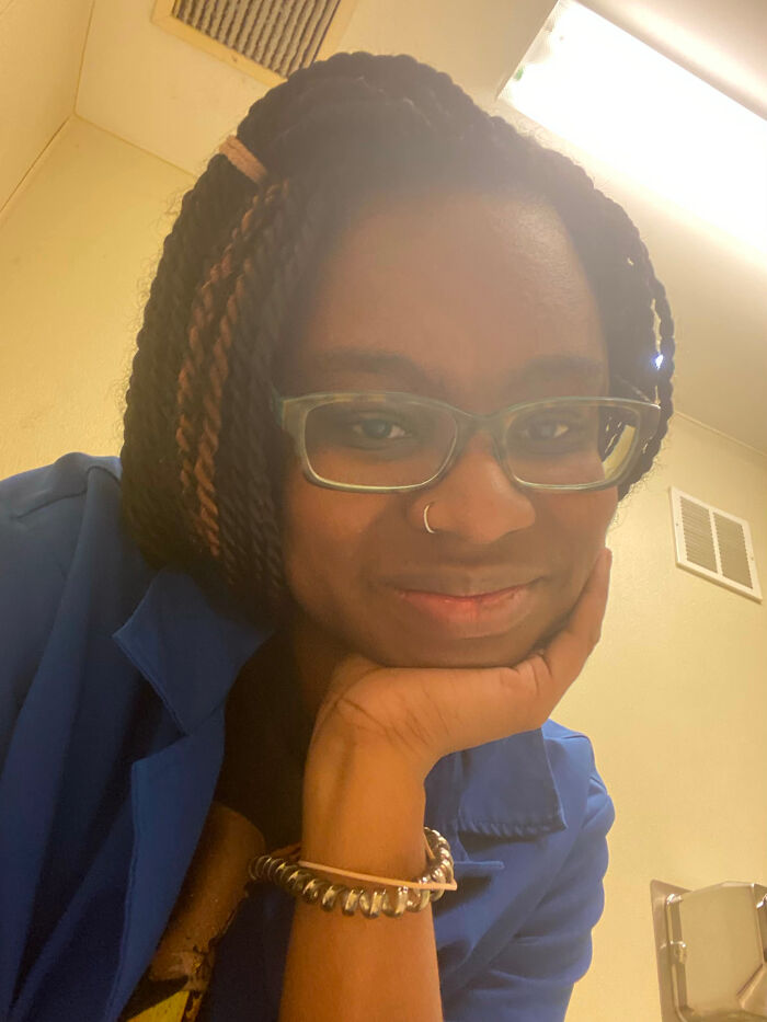 A woman with surprising facts about her looks, wearing glasses and a blue top, smiling at the camera.