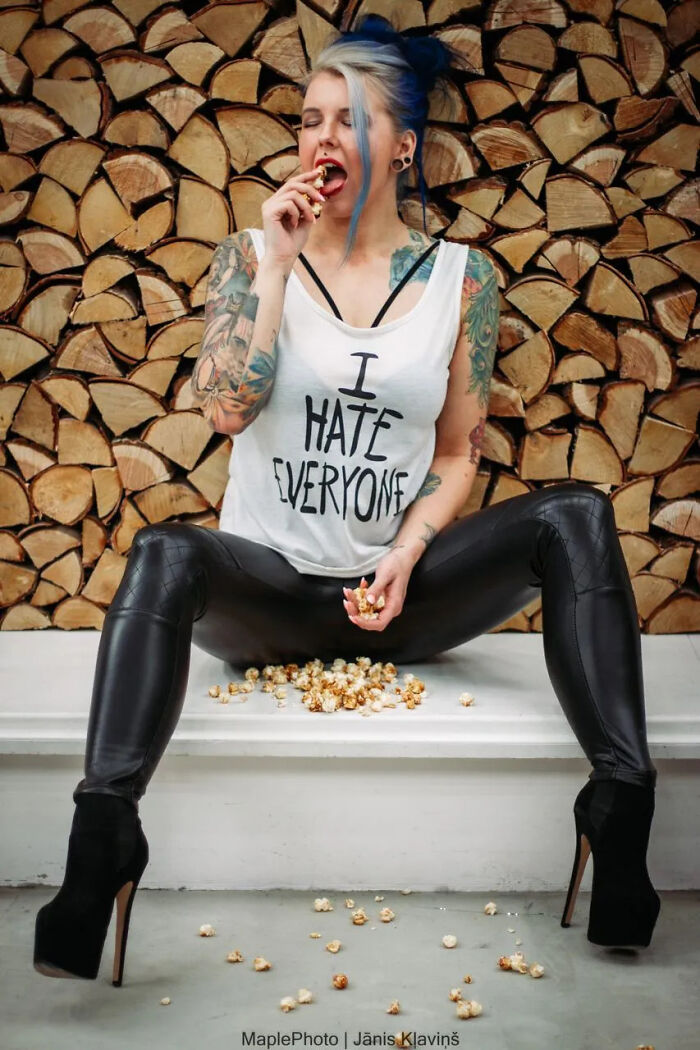 A woman with blue hair and tattoos, wearing a tank top and leather pants, eating popcorn, revealing surprising facts about people's looks.