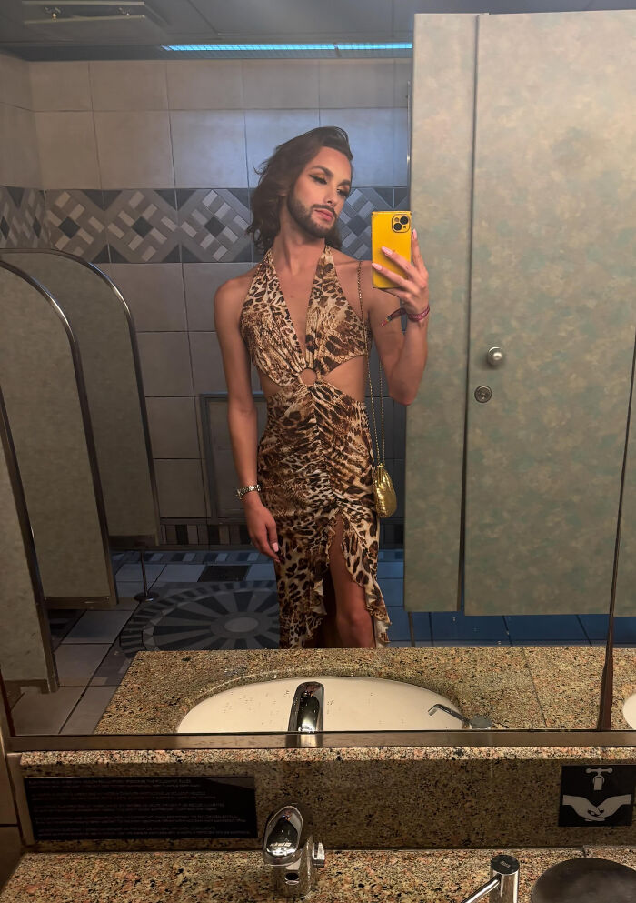 A person in a leopard print dress taking a mirror selfie in a public restroom, highlighting surprising facts about people's looks.