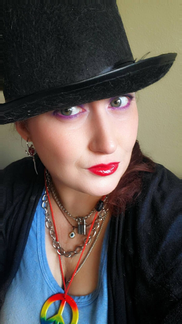 A woman wearing a top hat and bright makeup, featuring layered necklaces, illustrating surprising facts about people's looks.