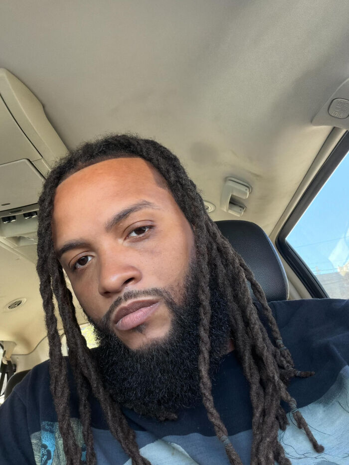 A man with dreadlocks and a beard, looking at the camera from inside a car. This image contains surprising facts.