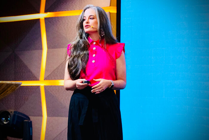 A woman with long gray hair speaking on stage, revealing surprising facts that dont match people's looks.