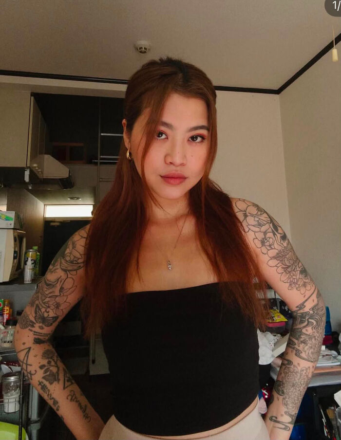 A woman with tattoos on both arms, a surprising fact that doesn't match her looks at all, posing indoors.