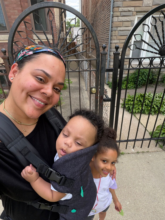 A woman smiling with a baby in a carrier and a young girl beside her. Surprising facts about people's looks.