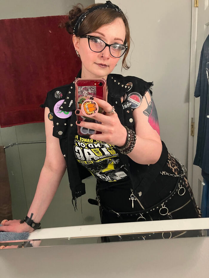 A woman with a studded vest and glasses taking a mirror selfie. Surprising facts about people's looks.