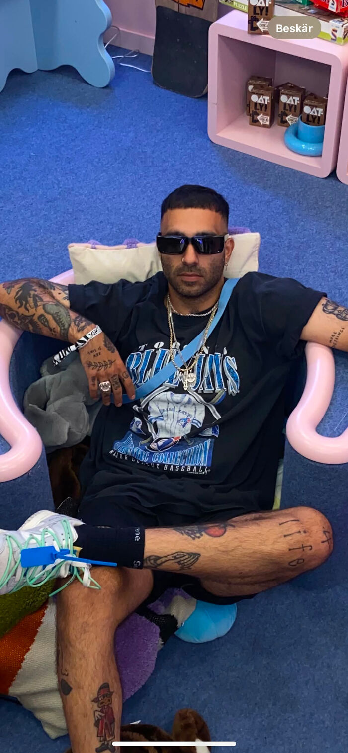 A man with tattoos and sunglasses sitting in a chair, showcasing surprising facts that dont match his looks.