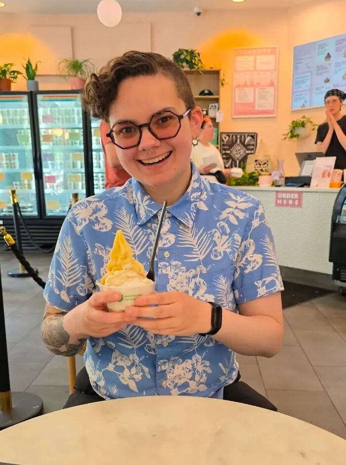 A person with glasses and a blue floral shirt smiling while holding a cup of ice cream, showing surprising facts.