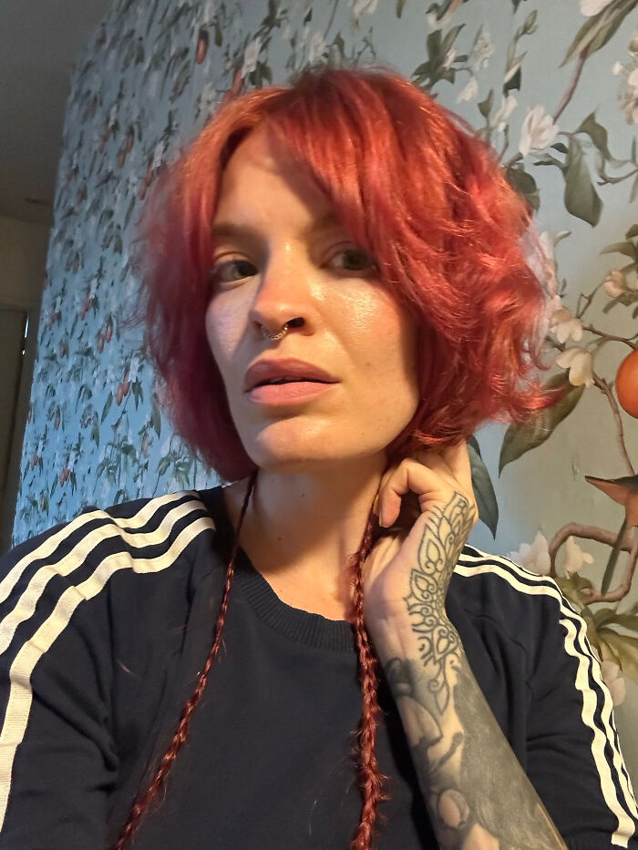 A woman with short red hair and a nose ring, with a tattooed arm, embodying surprising facts about people's looks.