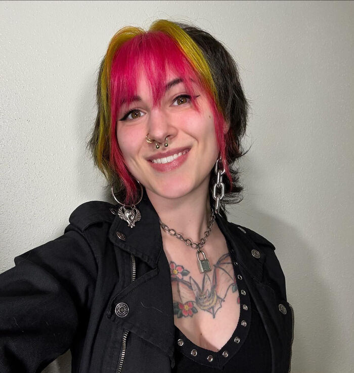 A smiling woman with pink and yellow hair, piercings, and tattoos, showcasing surprising facts about people's looks.