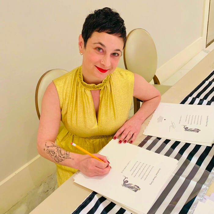 A woman with short dark hair and red lipstick, writing at a table, highlighting surprising facts about people's looks.