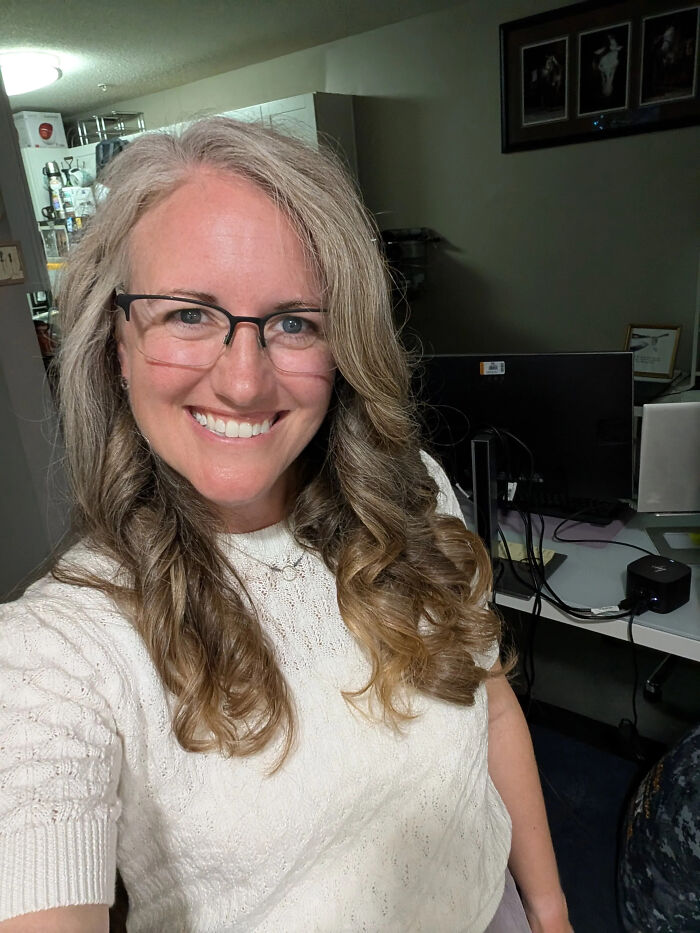 A smiling woman with glasses and long, wavy hair, showcasing surprising facts about people's looks.