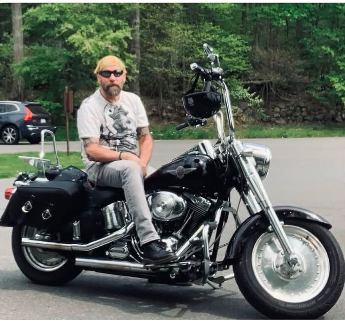 A man with a beard and sunglasses on a motorcycle, challenging people's looks and assumptions.