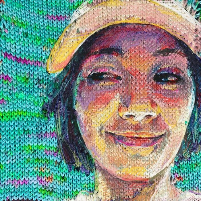 A vibrant modern art portrait of a smiling woman in a hat, created with traditional knitting techniques.