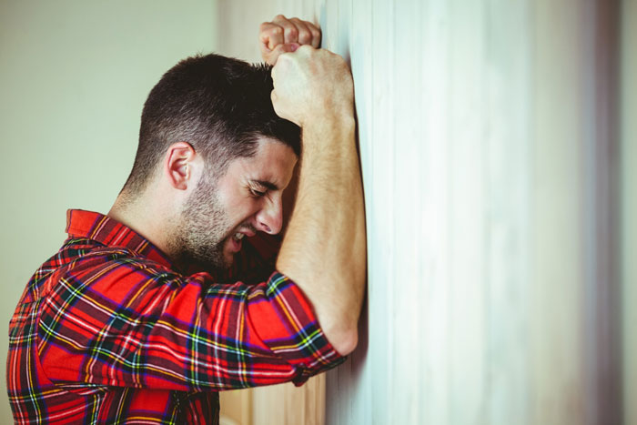 A man in a red plaid shirt, crying and hitting his head against a wall, depicting a boyfriend's distress. A man in a red plaid shirt, crying and hitting his head against a wall, depicting a boyfriend's distress.