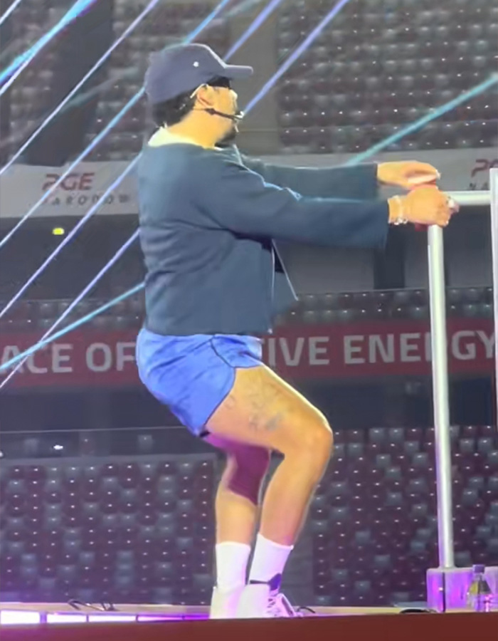 Bad Bunny on stage performing a steamy dance move in blue shorts and a dark top, fans lose it. Bad Bunny on stage performing a steamy dance move in blue shorts and a dark top, fans lose it.