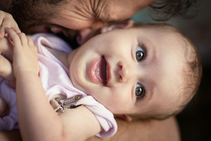 A close-up of a smiling baby daughter, held by her dad. Dads with daughters often have their understanding of women changed.