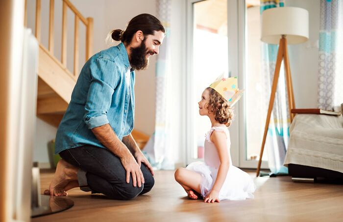 A dad kneeling, smiling at his daughter in a crown, illustrating how dads views of women changed.