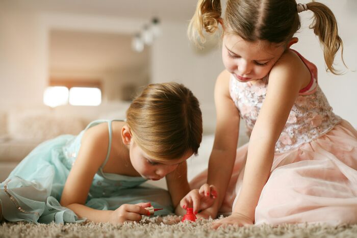 Two young daughters playing together on a rug, painting nails. Dads with daughters see women in a new light.