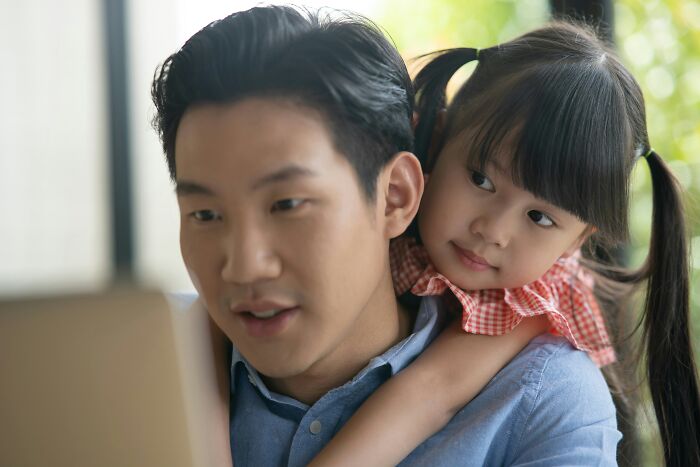 A dad working on a laptop with his daughter hugging him from behind. Dads who had daughters changed their view and understanding of women.