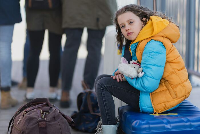 A young girl sitting on a suitcase, holding a toy. Dads who had daughters changed their view and understanding of women.