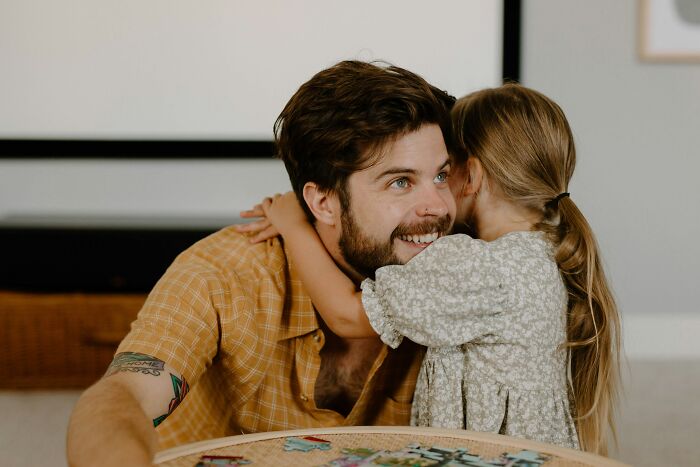 A dad smiling as his daughter whispers in his ear. Dads who had daughters changed their view and understanding of women.