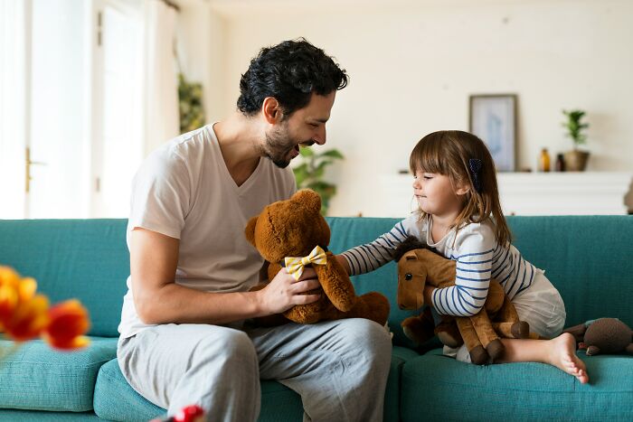 A dad and his daughter playing with stuffed animals on a sofa. Dads who had daughters changed their view and understanding of women.