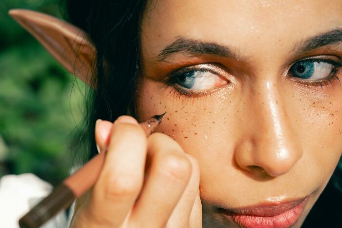 A person with elf ears applying makeup to create freckles, representing strange jobs in entertainment.