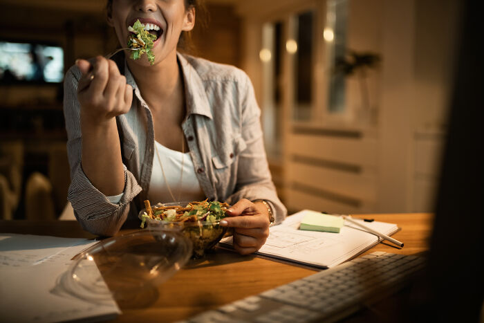 A person happily eating a salad at a desk, contrasting with stories of guests who ignored house etiquette.