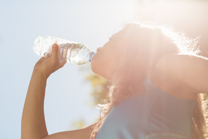 A person drinking water from a plastic bottle outdoors, possibly regretting spending money on bottled water.