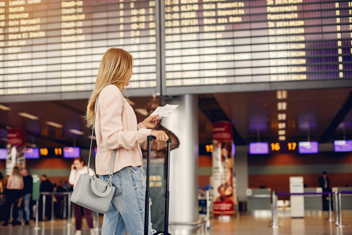 A young woman, an 18YO daughter, stands in an airport terminal with luggage, looking at a departure board, trying to leave the country. A young woman, an 18YO daughter, stands in an airport terminal with luggage, looking at a departure board, trying to leave the country.