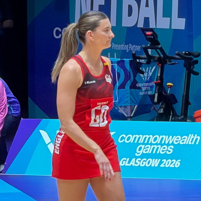 Female athlete in a red netball uniform, focused during a match, sparking discussion about unusual uniforms and malfunctions.