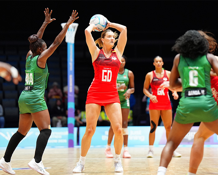 Female athletes in red and green uniforms playing netball, highlighting unusual uniforms and potential wardrobe malfunctions.