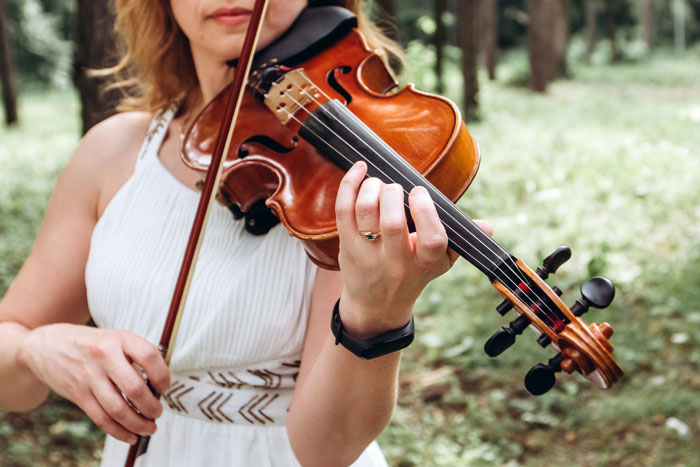 A close-up of a woman in a white dress playing a violin, representing the wedding music.