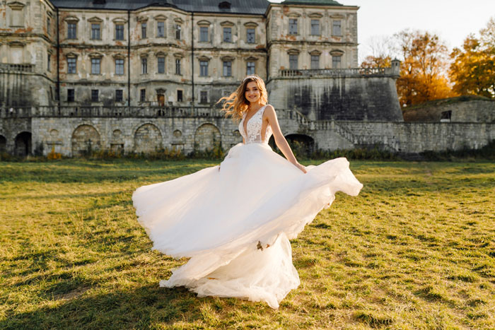 A beautiful bride in a flowing white wedding gown spinning joyfully in front of a grand castle.