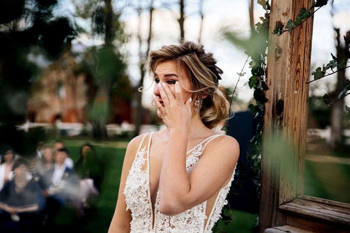 A close-up of a bride in a wedding dress, wiping away tears during her wedding ceremony.