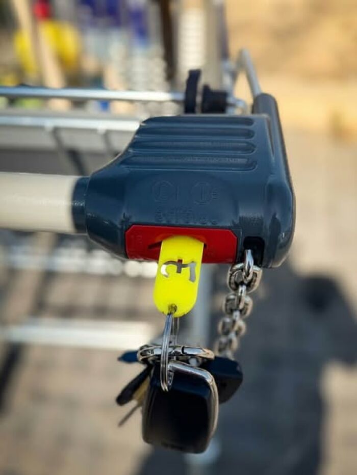A close-up of a 3D printer created shopping cart coin, with a set of keys attached, inserted into a cart handle.