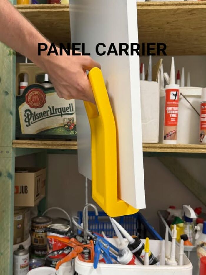 A person carries a white panel with a yellow 3D printer created panel carrier, in a workshop setting.
