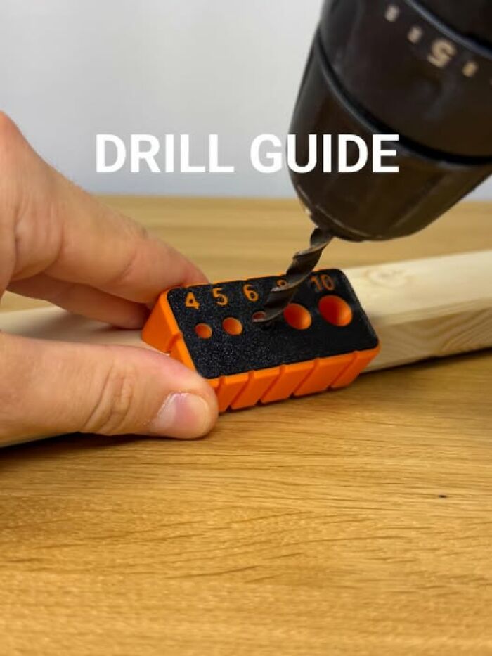 A hand holds a 3D printer drill guide on a wooden surface, demonstrating functional 3D printed objects.