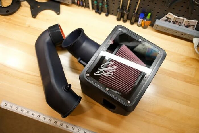 A 3D printer created car air intake system, showing a custom-made functional component on a wooden workbench.