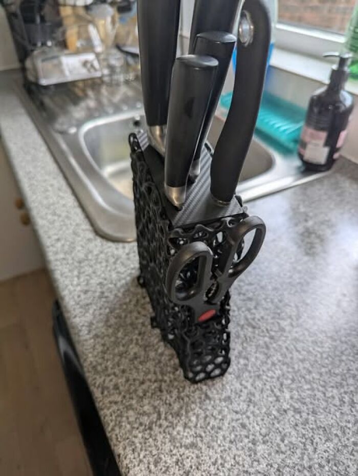 A black knife block, a functional and cool 3D printer creation, holds knives and scissors on a kitchen counter.